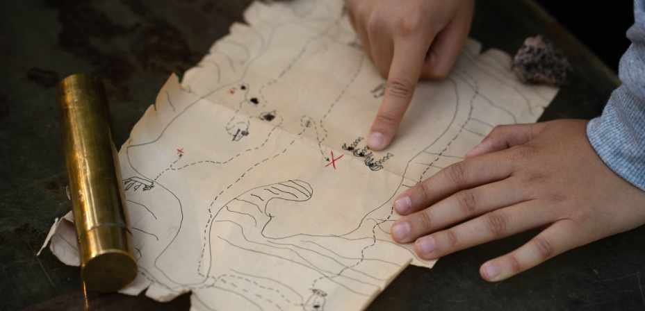 A child's hands pointing to an x on a treasure map. 