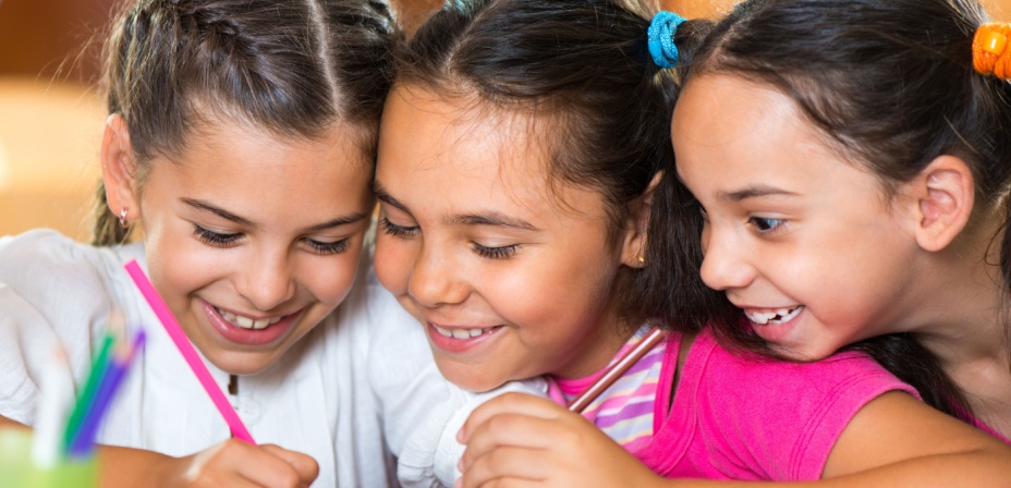 Three young girls smiling and laughing as they are writing a rhyming story together. 