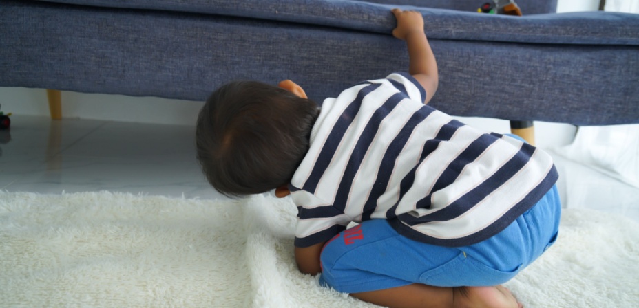 Young boy looking under the couch for something. 