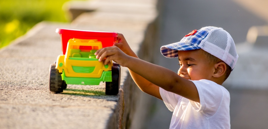 A child driving a dump truck toy along the concrete outside on a sunny day.