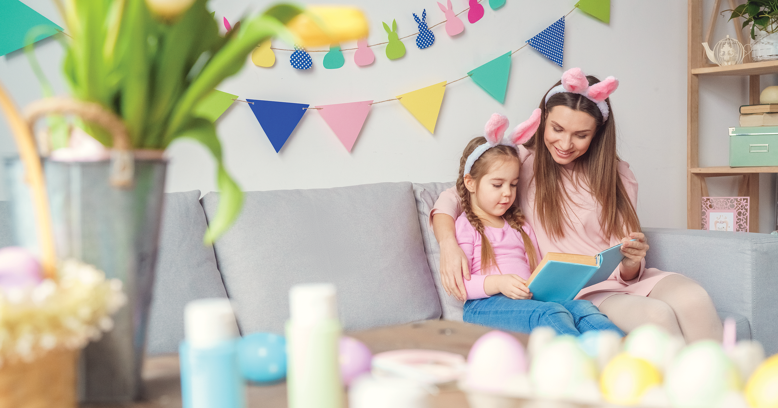 A mother and daughter sitting on the couch reading a book of Easter poems together. 