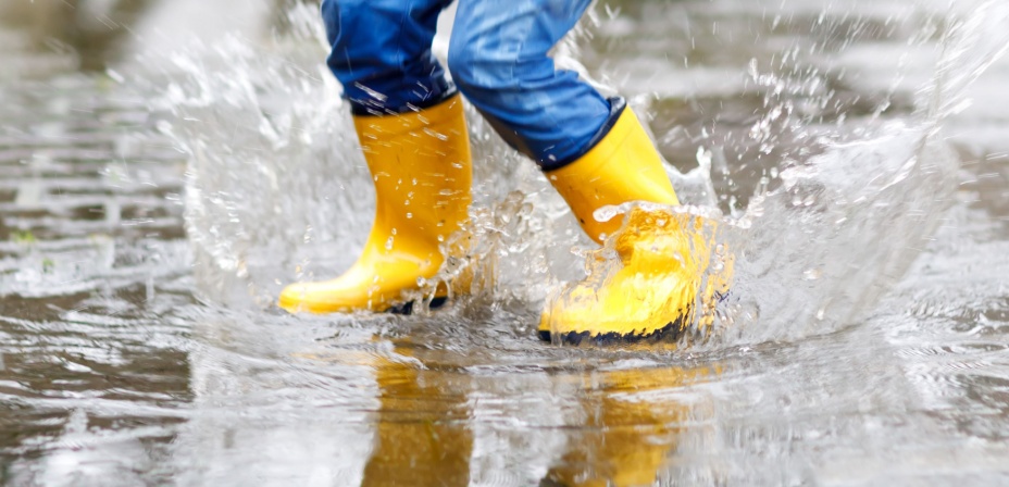 A child's legs with rain boots jumping in puddles for a fun spring activity for kids. 